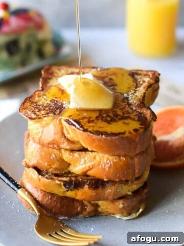 Straight on view of orange and cardamom french toast with maple syrup being poured from above on a grey background
