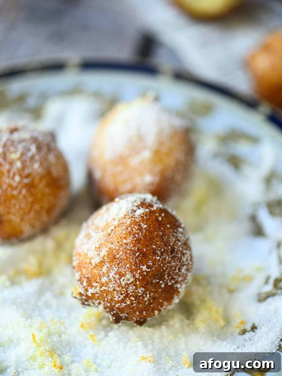 Orange Ricotta Zeppole: Classic Italian Ricotta Doughnut Recipe 4 Donut being rolled in a plate of orange sugar.