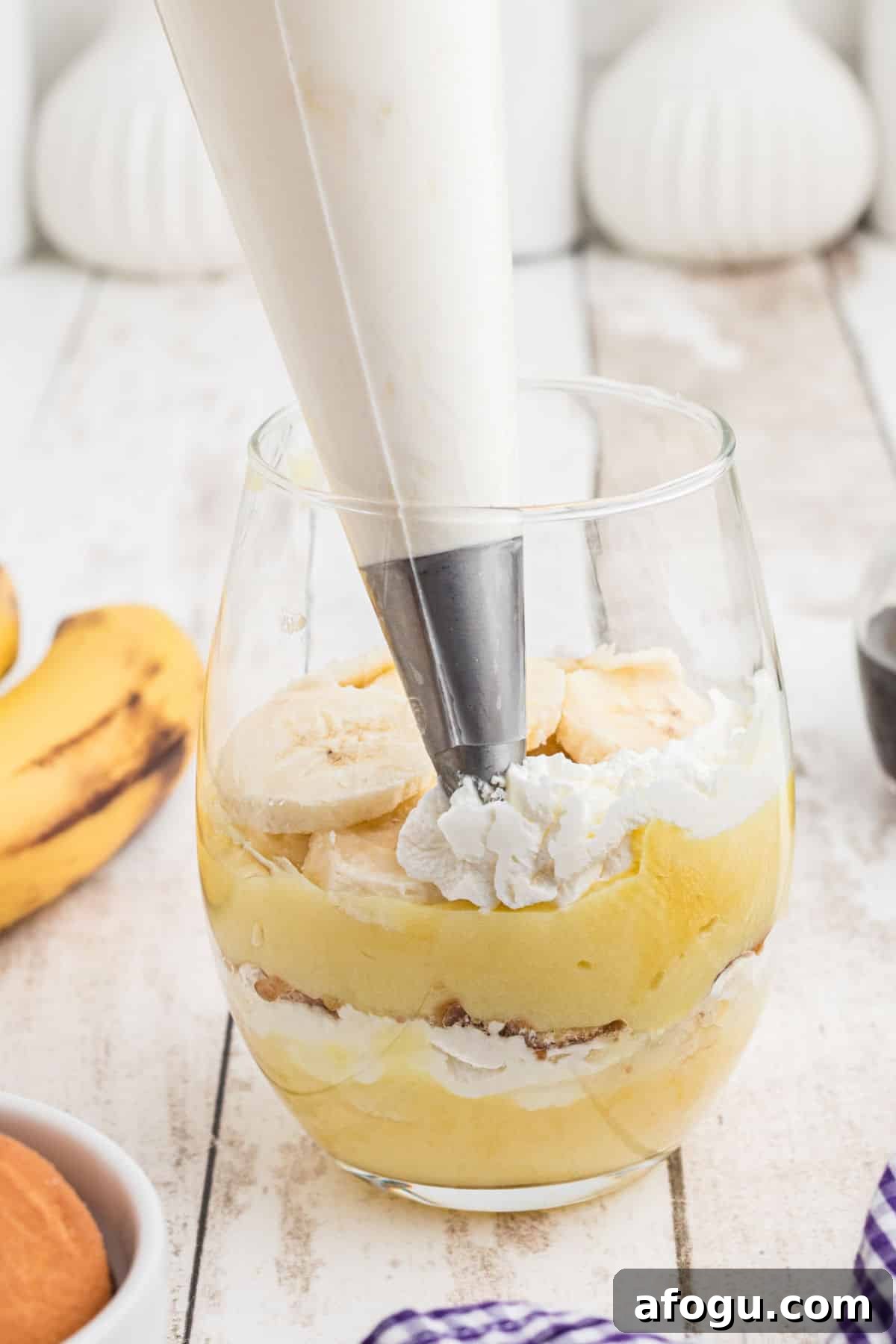 A glass being filled in layers making banana pudding cups.