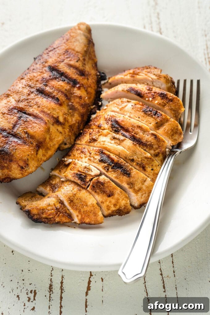 Slices of grilled chicken with dark grill marks on a plate with a fork.