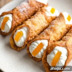 Homemade Sicilian Cannoli Recipe: Crispy Shells & Ricotta Filling 10 A close up of four homemade cannoli filled with ricotta and topped with candied orange on a plate