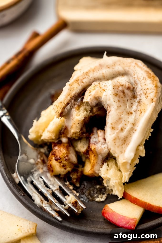 Aerial photo of an apple cinnamon roll on a plate with a fork and a bite taken out of the roll.
