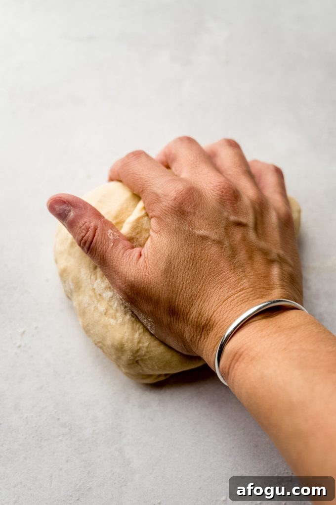 Someone's hand kneading yeasted cinnamon roll dough on a surface.