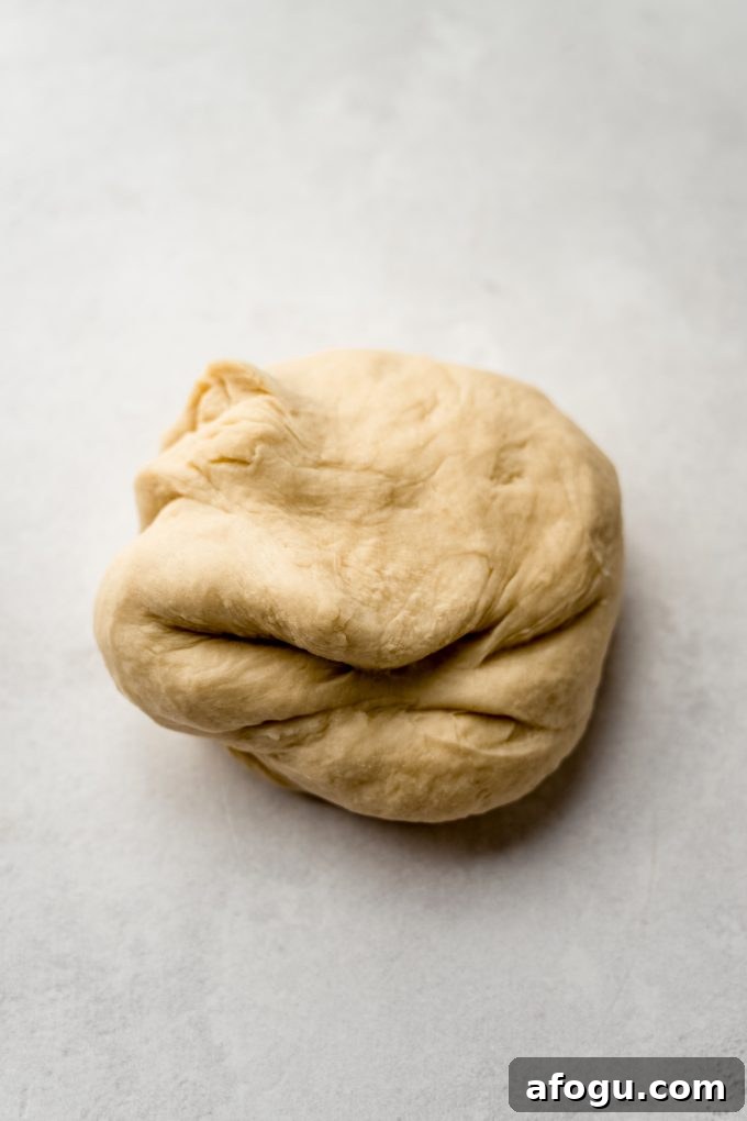 A ball of smooth yeasted cinnamon roll dough on s surface.