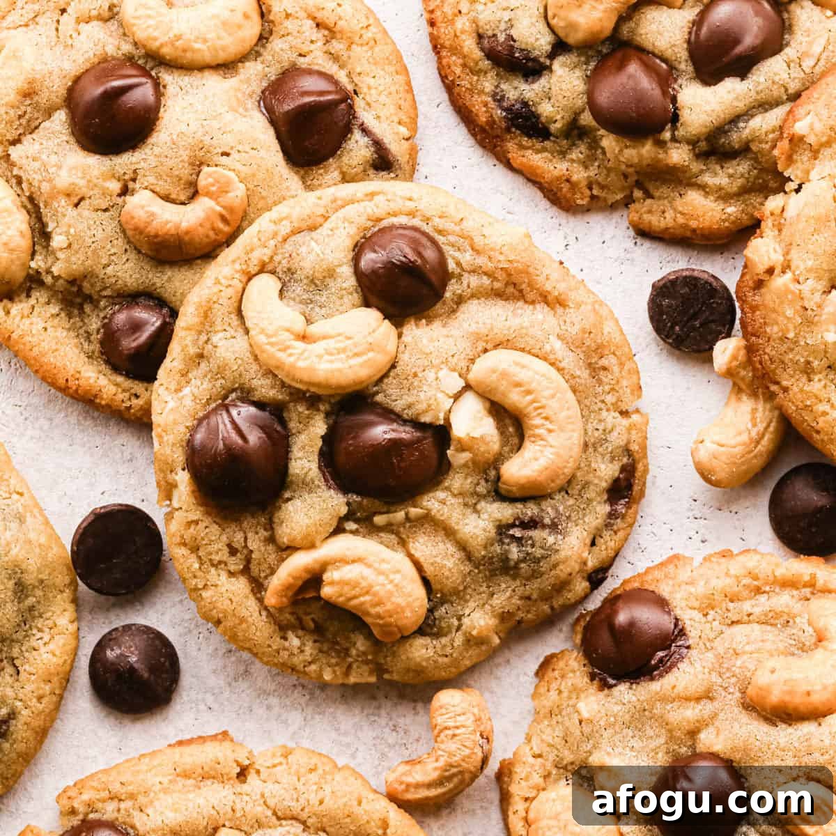 Chocolate Chip Cashew Cookies Recipe — Crunchy Homemade Treats 2 Overhead photo of golden-brown chocolate chip cashew cookies on parchment paper, studded with large chocolate chips and whole roasted cashews, with a few loose chocolate chips and cashews scattered around the cookies.