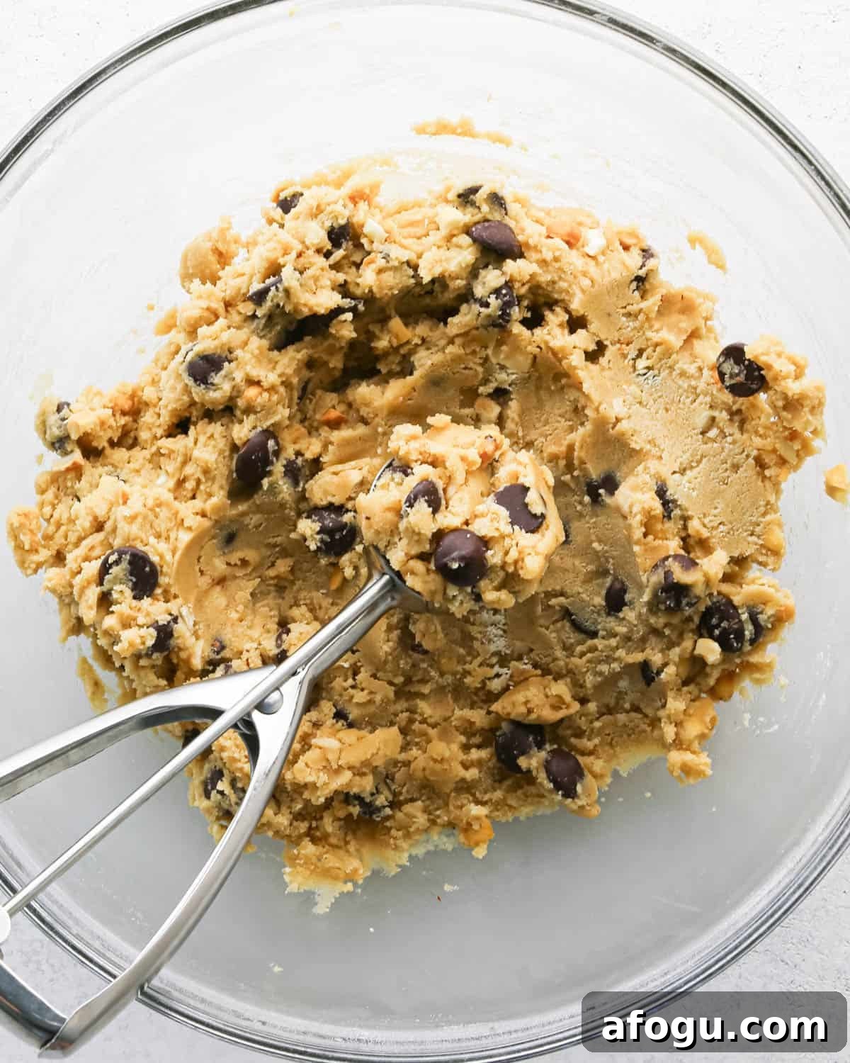 Chocolate Chip Cashew Cookies Recipe — Crunchy Homemade Treats 16 Making chocolate chip cashew cookies: overhead photo of a mixing bowl with prepared cookie dough. The cookie dough is being scooped with a cookie scoop.