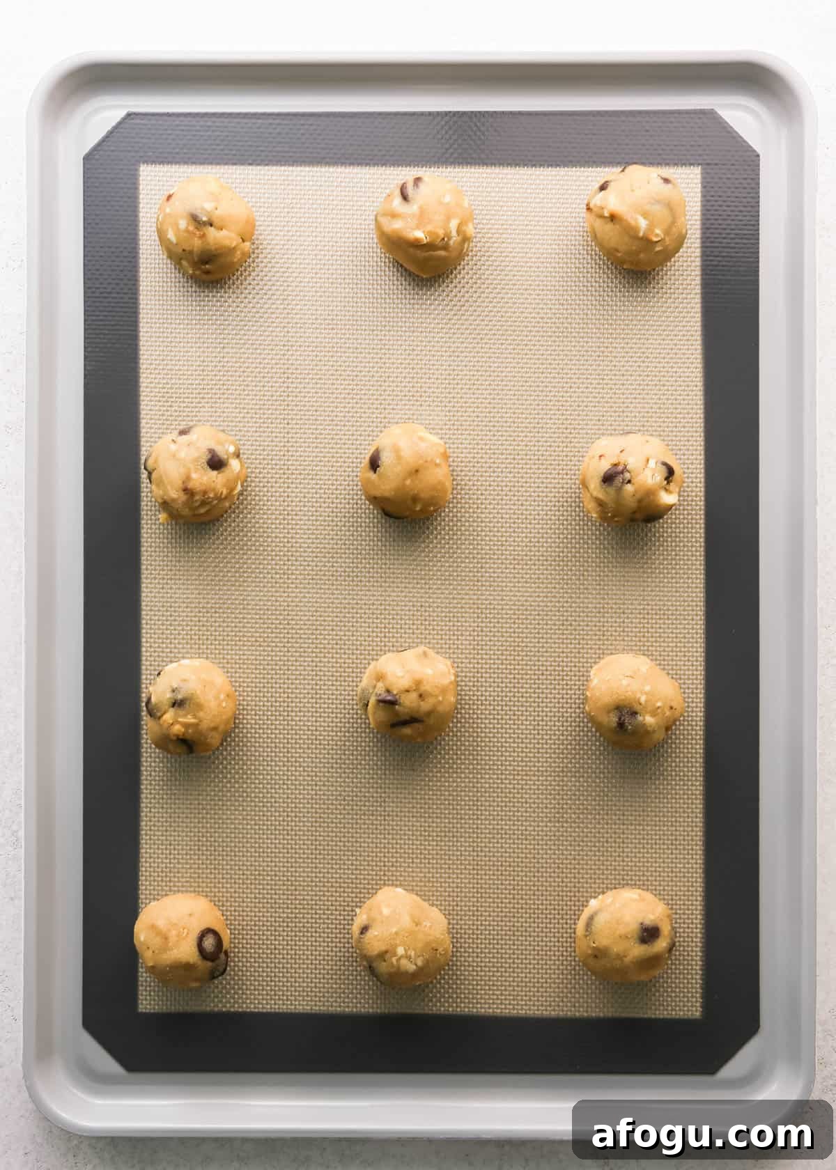 Chocolate Chip Cashew Cookies Recipe — Crunchy Homemade Treats 17 Making chocolate chip cashew cookies: overhead photo of 12 balls of cookie dough scooped, rolled, and placed onto a baking sheet on a countertop.