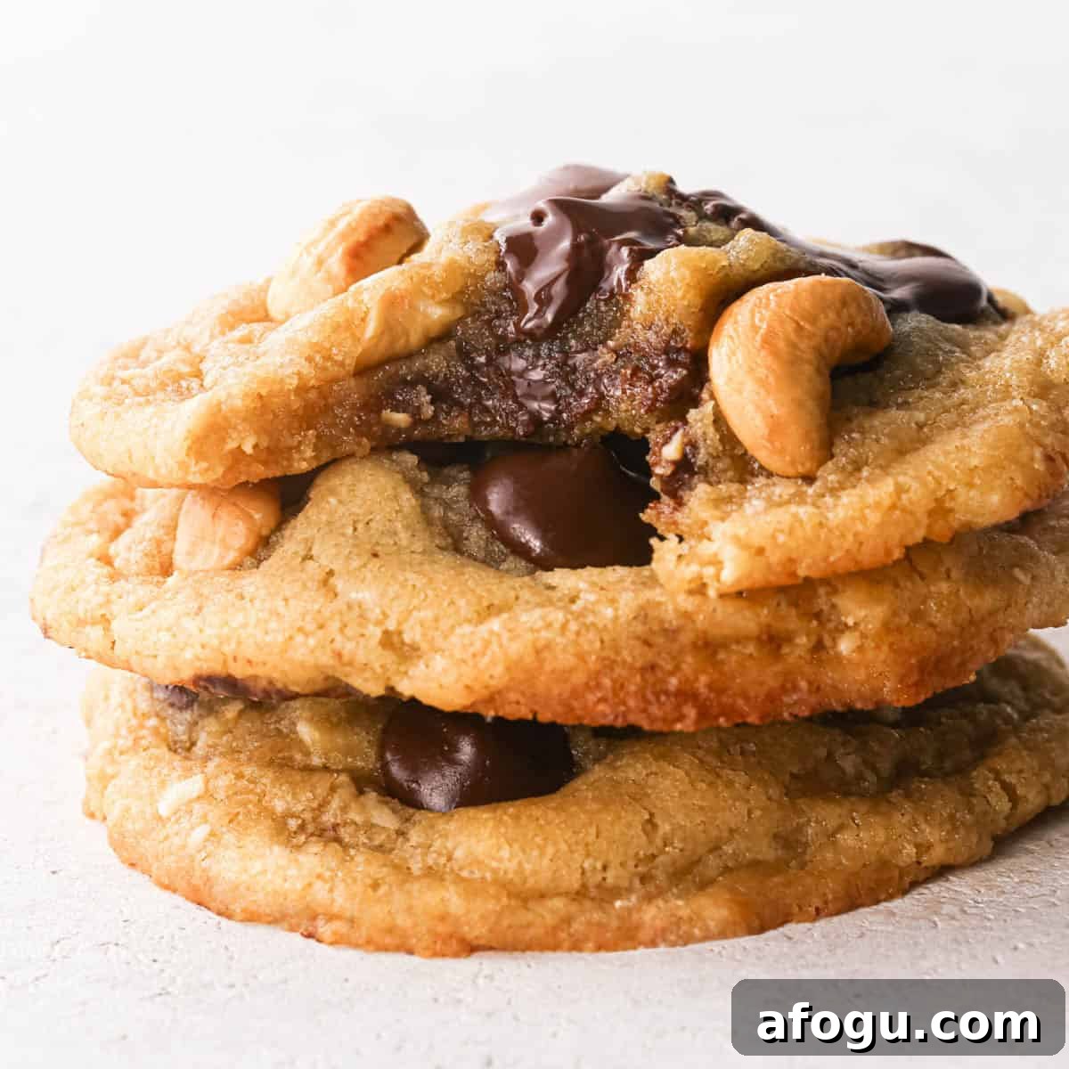 Chocolate Chip Cashew Cookies Recipe — Crunchy Homemade Treats 3 Close-up photo of a stack of 3 golden-brown chocolate chip cashew cookies on a white surface, studded with large chocolate chips and whole roasted cashews.