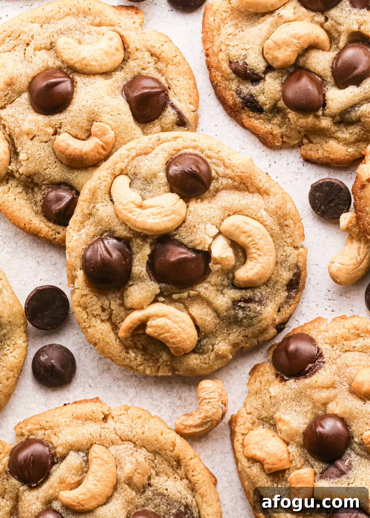 Chocolate Chip Cashew Cookies Recipe — Crunchy Homemade Treats 20 Overhead photo of golden-brown chocolate chip cashew cookies on parchment paper, studded with large chocolate chips and whole roasted cashews, with a few loose chocolate chips and cashews scattered around the cookies.