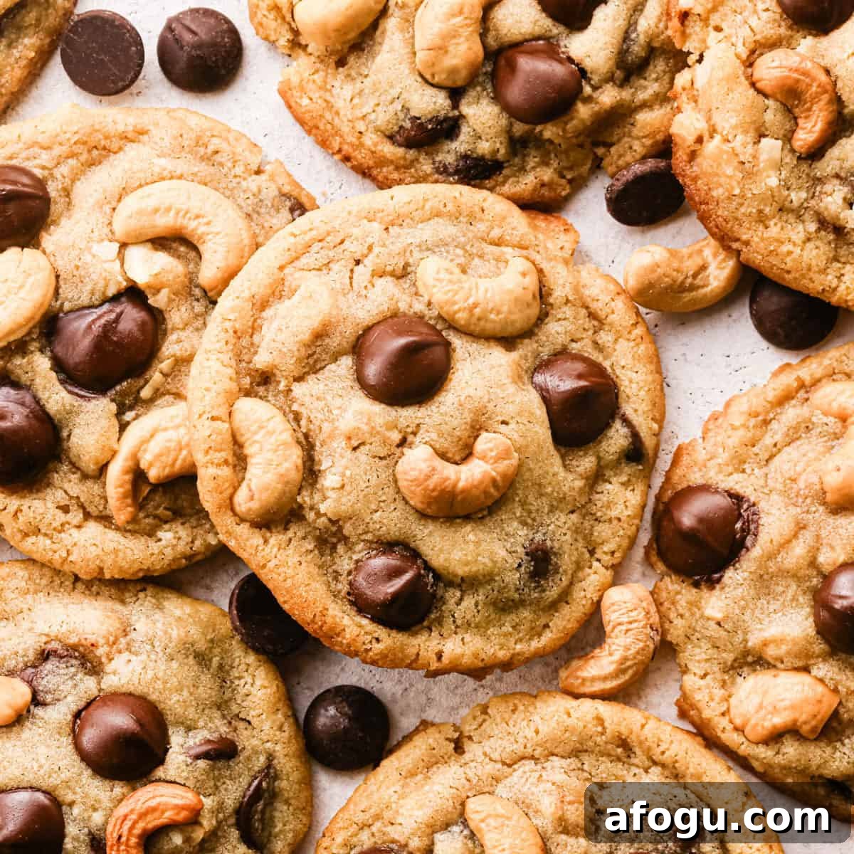 Chocolate Chip Cashew Cookies Recipe — Crunchy Homemade Treats 5 Overhead photo of golden-brown chocolate chip cashew cookies on parchment paper, studded with large chocolate chips and whole roasted cashews, with a few loose chocolate chips and cashews scattered around the cookies.