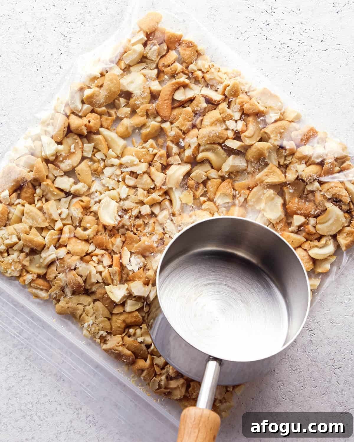 Chocolate Chip Cashew Cookies Recipe — Crunchy Homemade Treats 8 Making chocolate chip cashew cookies: overhead photo of a gallon plastic bag filled with cashews and being crushed inside the bag with a metal measuring cup.