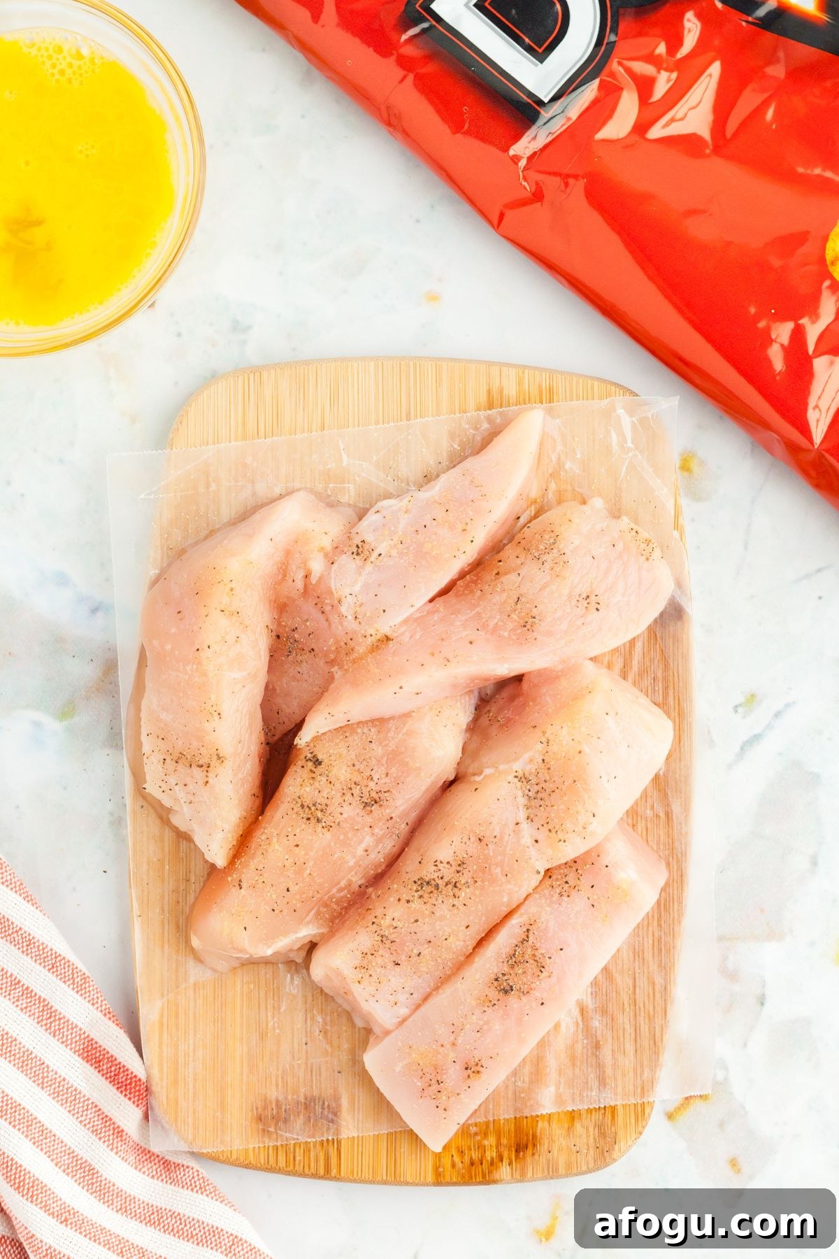 Crispy Dorito-Crusted Air Fryer Chicken Recipe 4 Chicken tenders seasoned and a bag of dortios on a marble board
