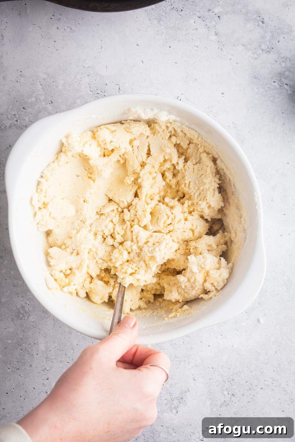 A hand mixing cornbread dough in a white bowl.