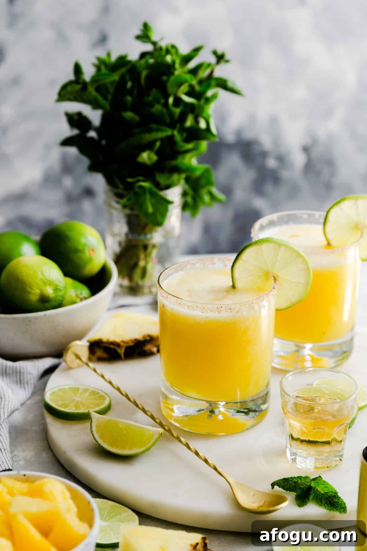 two glasses with pineapple margaritas on a marble chopping board