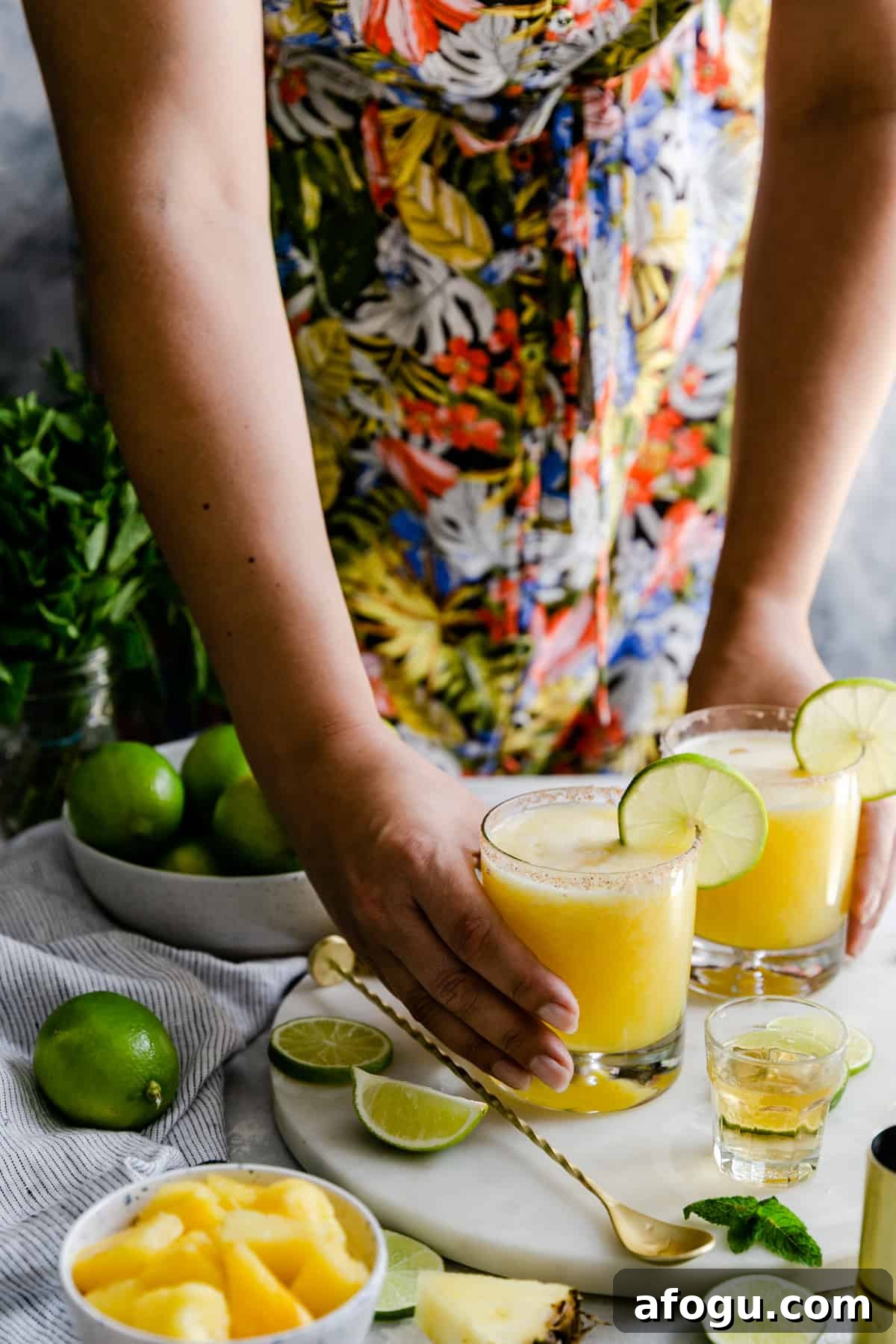 a person holding two glasses of frozen pineapple margaritas