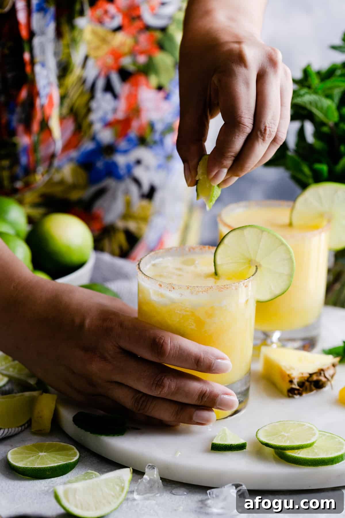 a person squeezing a lime slice into a cocktail