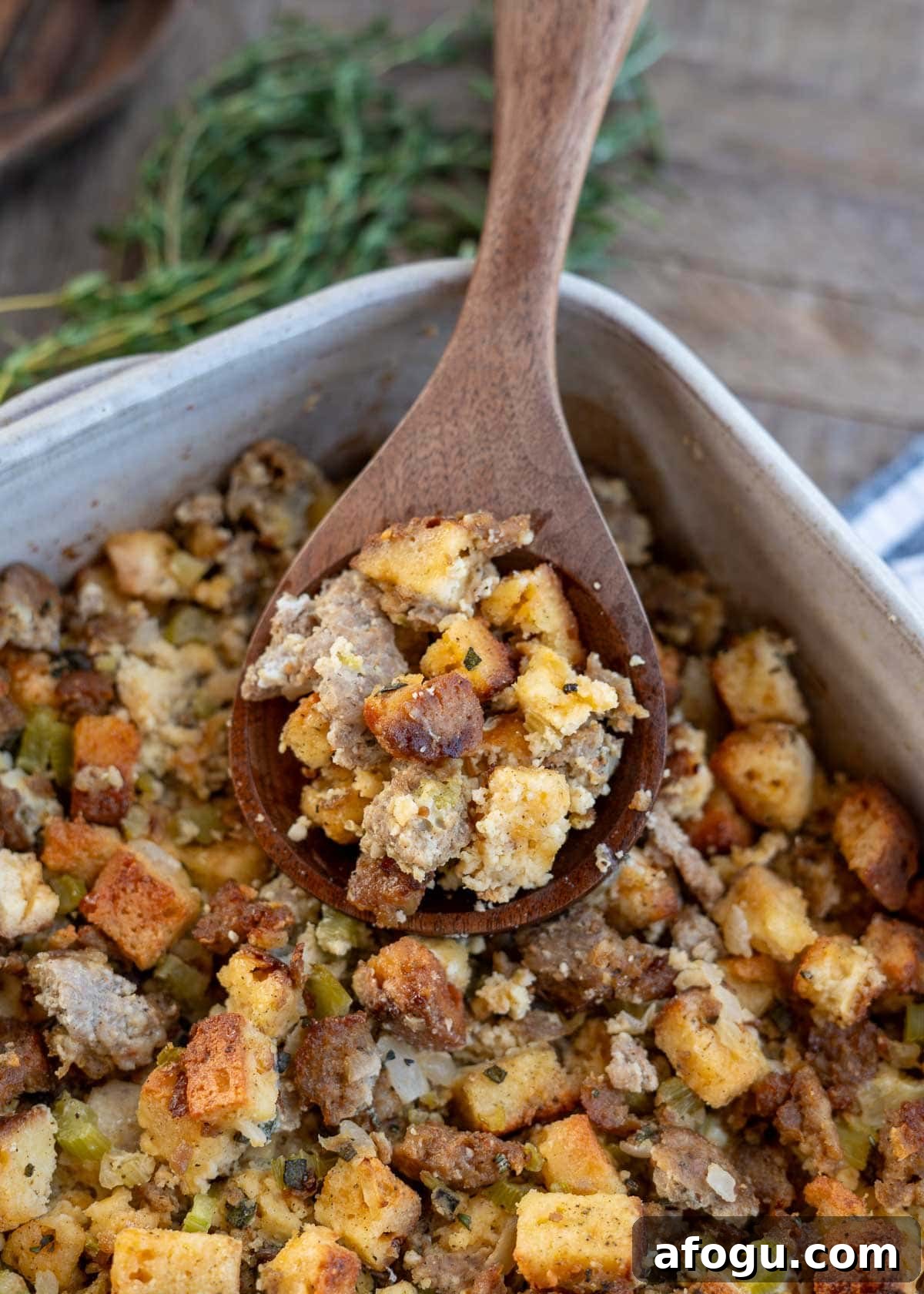 an overhead shot of sausage stuffing in a dish with a brown spoon and herbs on the side.