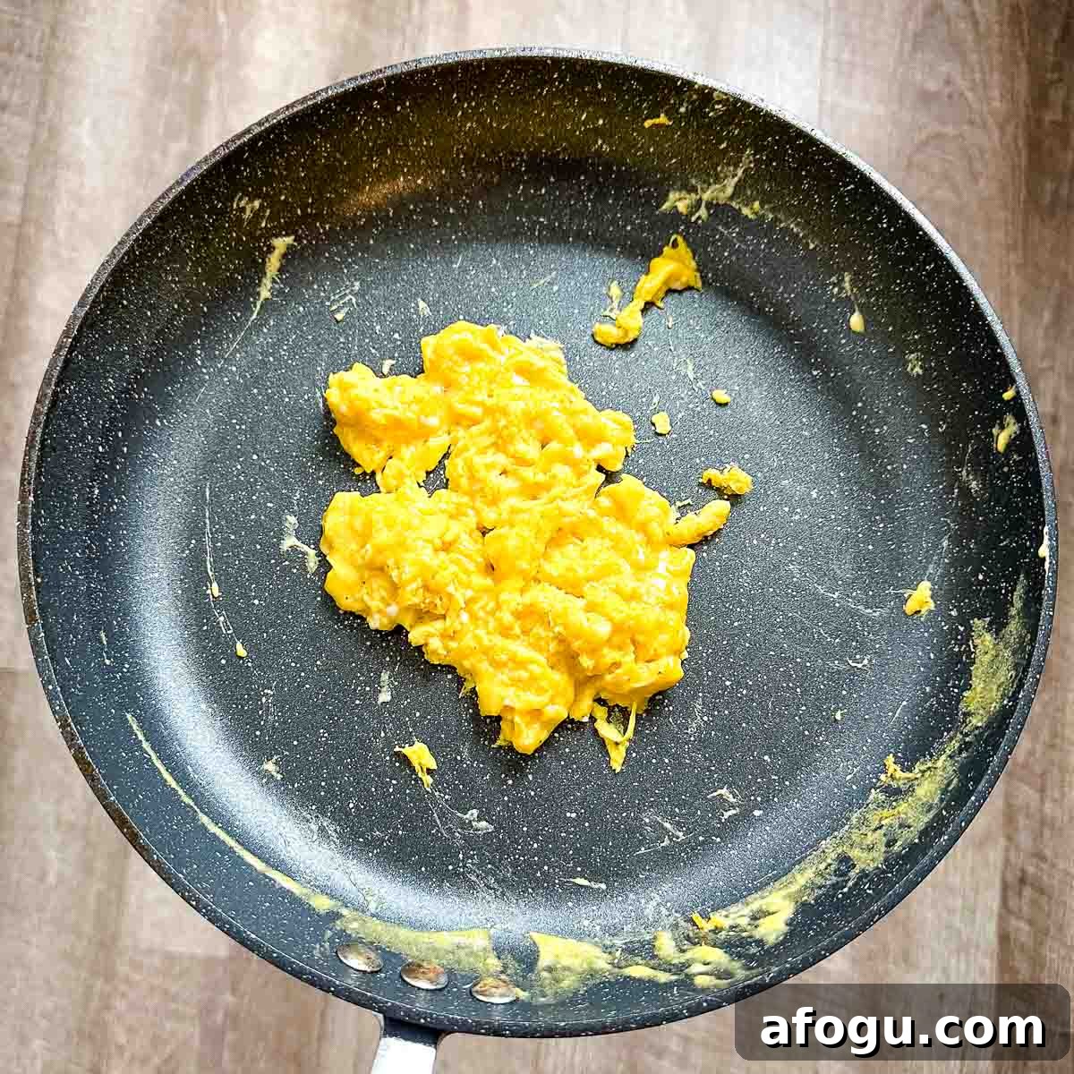 Cooked cheesy scrambled eggs sit in a black frying pan.