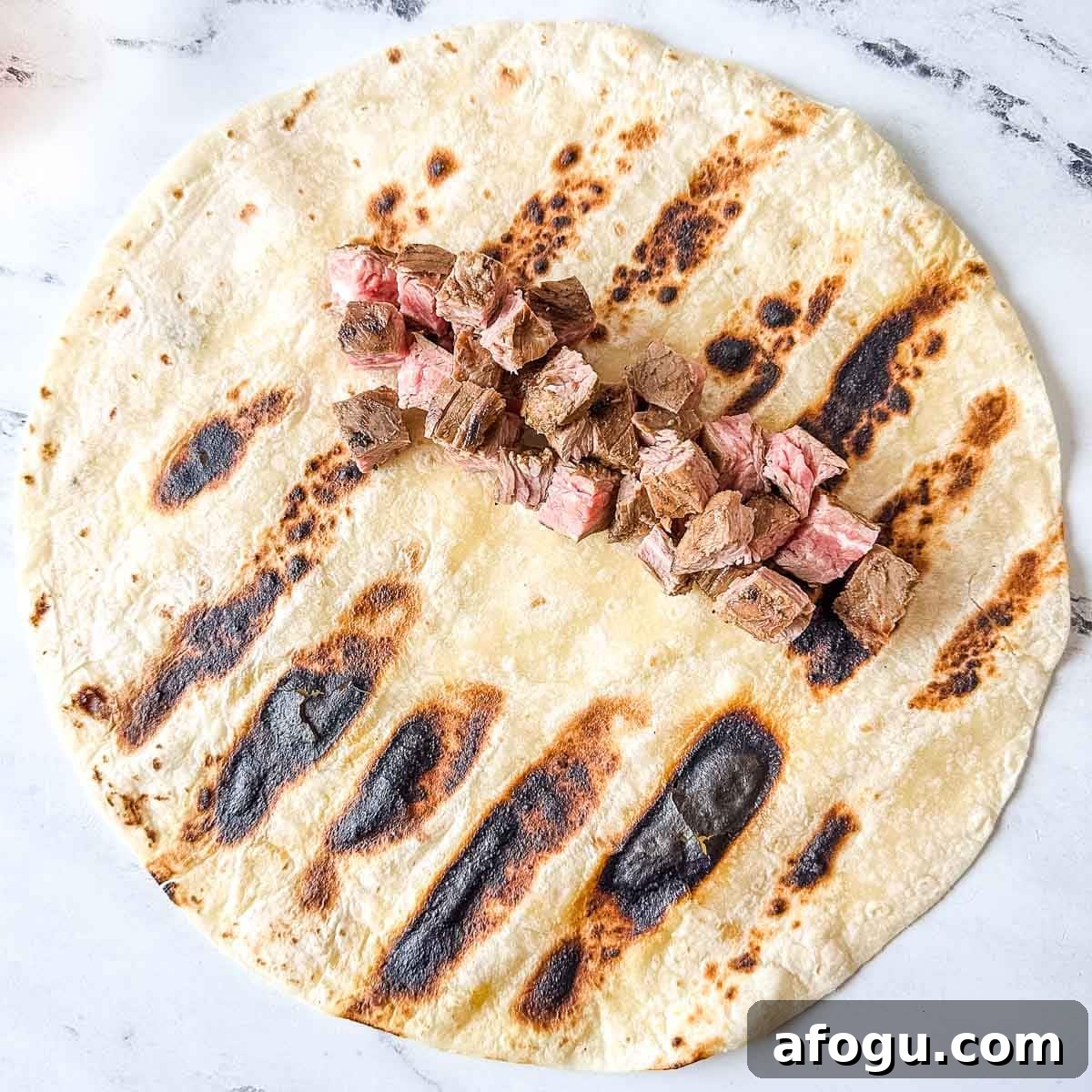 Diced carne asada pieces sit on top of a grilled tortilla.