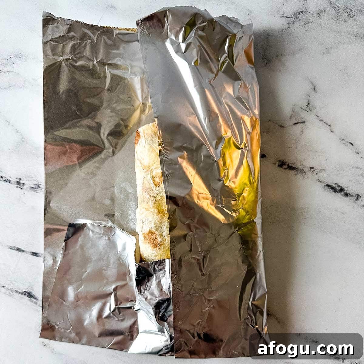 The bottom portion of the foil and the right vertical edge of foil are folded over the carne asada burrito.