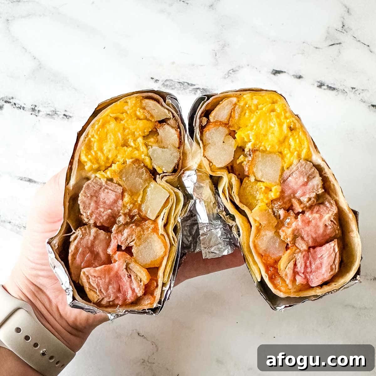 Carne asada burrito that is wrapped in foil and cut in half to expose the center of the burrito.