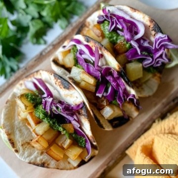 Three Spicy Potato Soft Tacos sit on a wooden cutting board surrounded by a yellow linen and parsley.