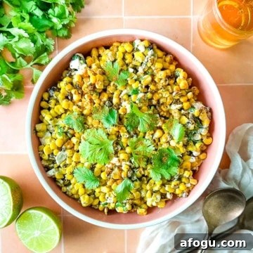 Overhead shot of an elote bowl surrounded by halved limes, cilantro, a cup of beer, and a white linen.