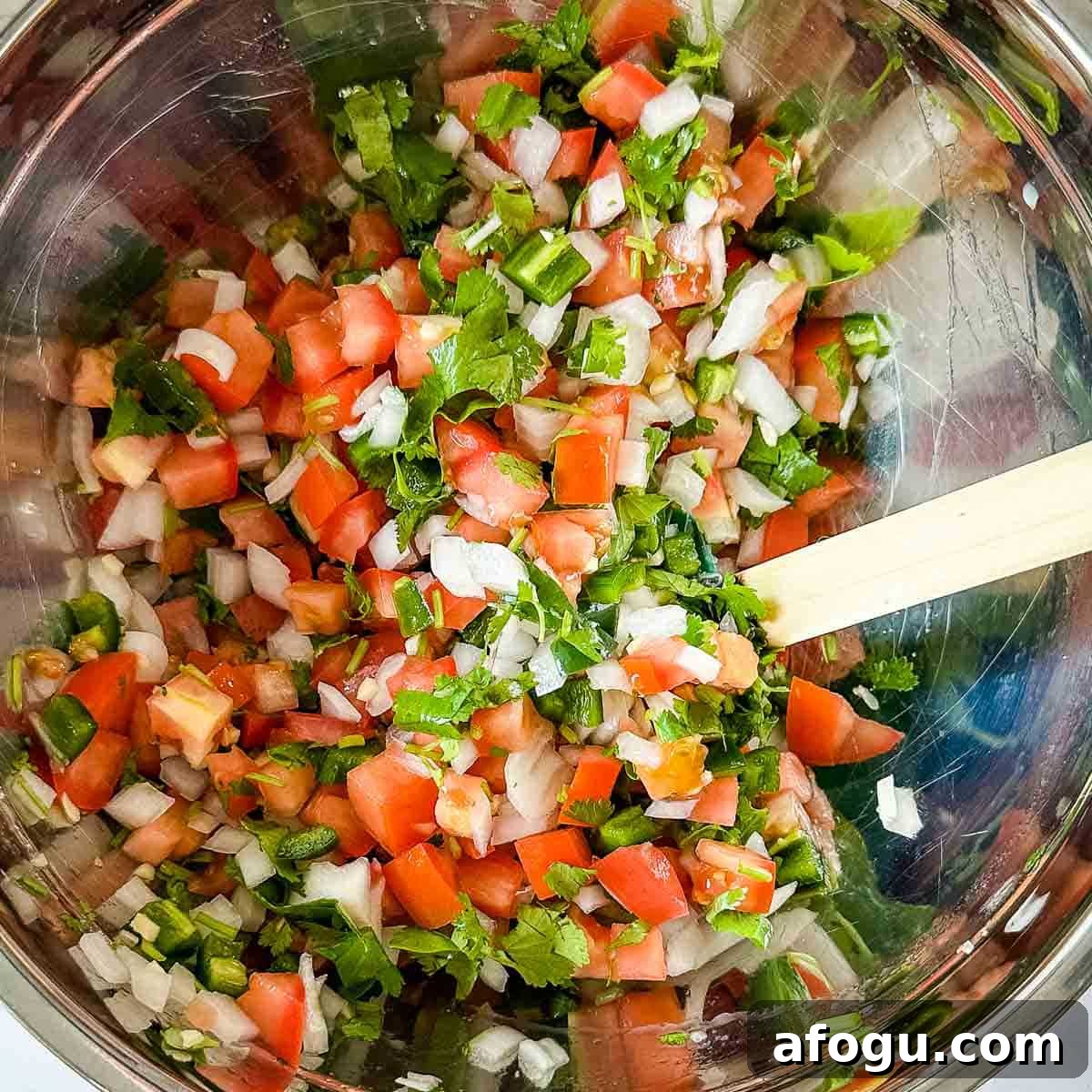 Garden fresh salsa is mixed in a stainless steel bowl.