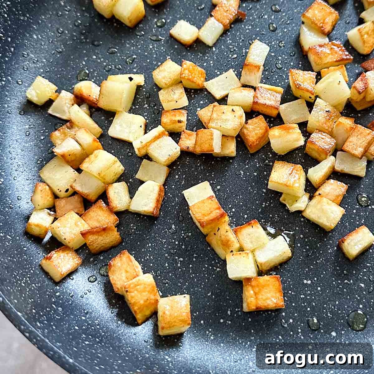 Fully cooked diced potatoes are shown in a black frying pan.