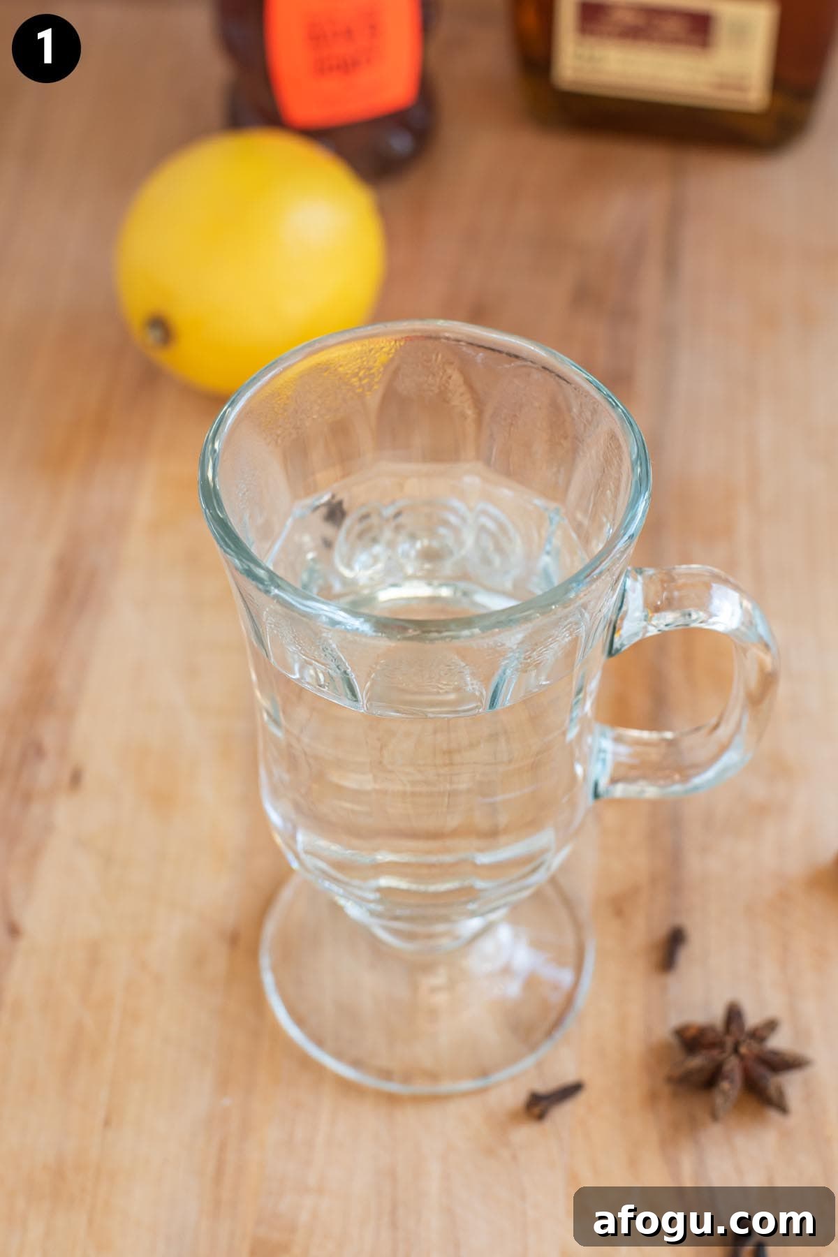 Hot water in a glass mug on a wooden cutting board with a lemon in the background.
