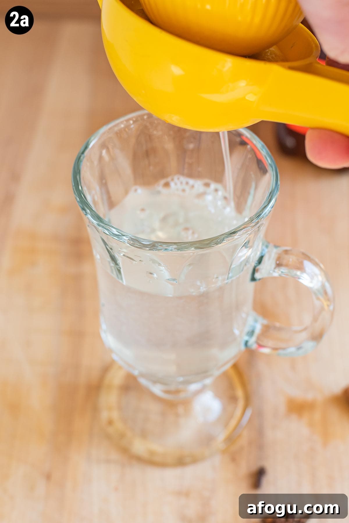Squeezing lemon juice into a mug with hot water with a citrus squeezer.