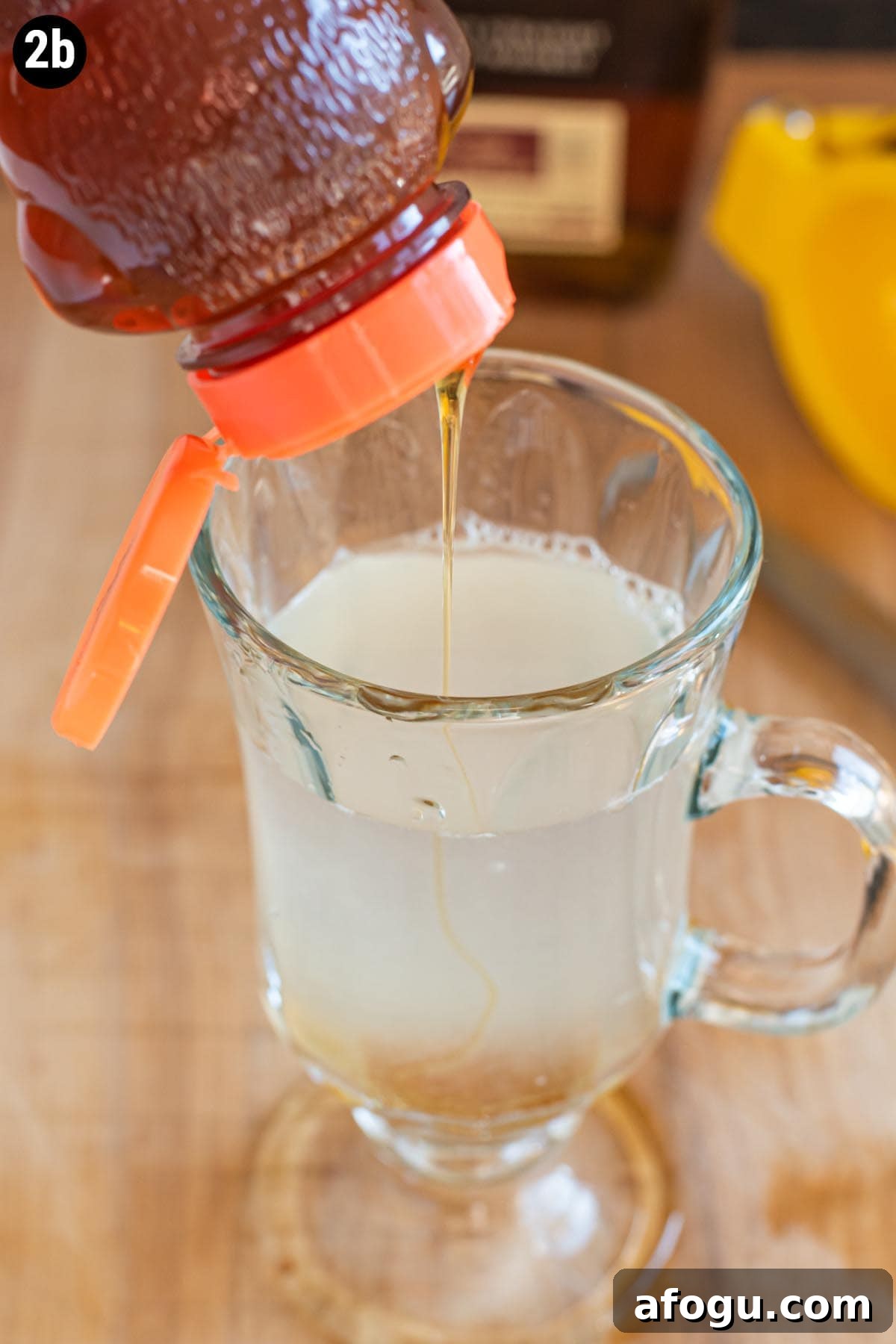 Pouring honey into a glass mug filled with hot water and fresh lemon juice.