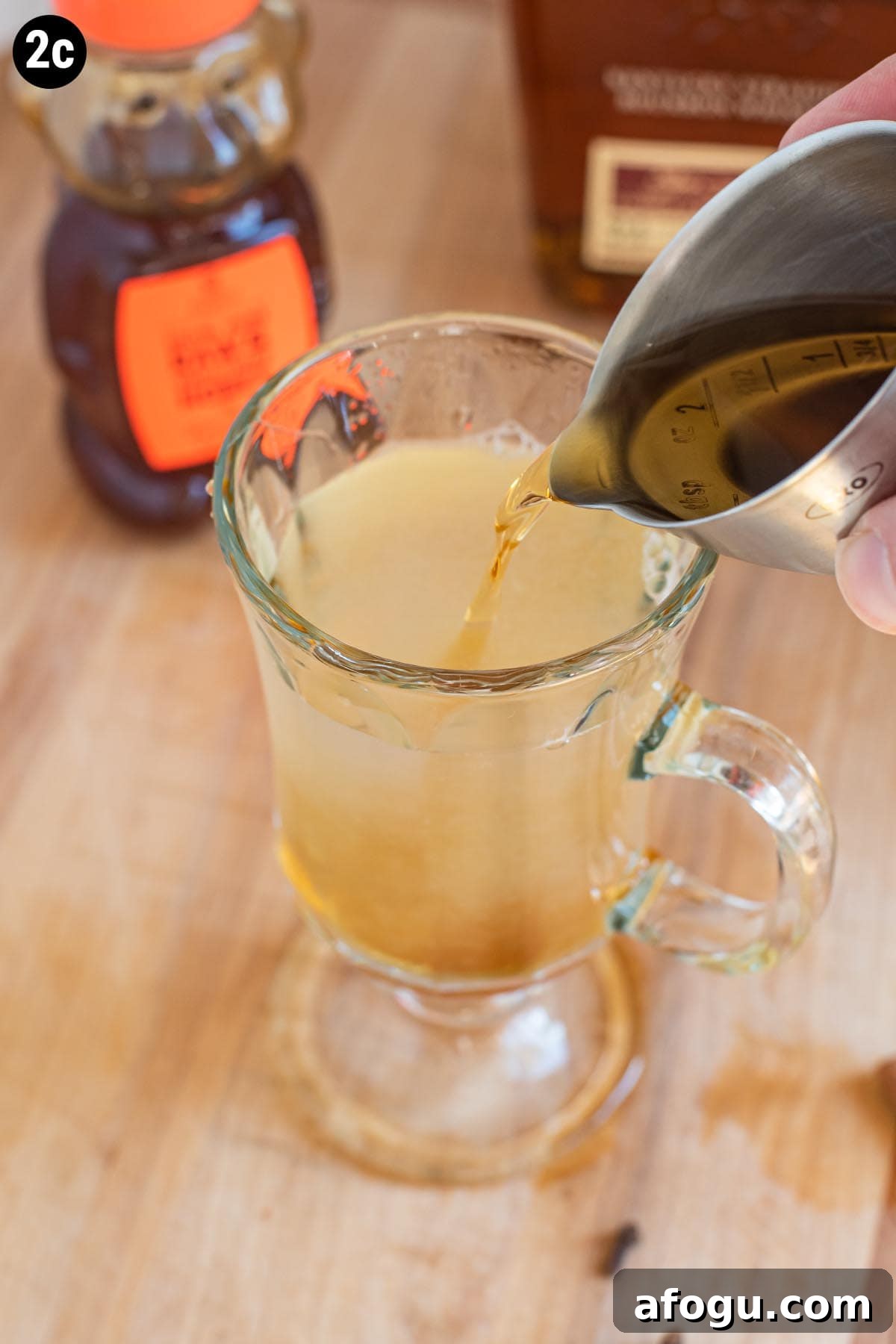 Adding a jigger of bourbon to a Hot Toddy cocktail on a cutting board.
