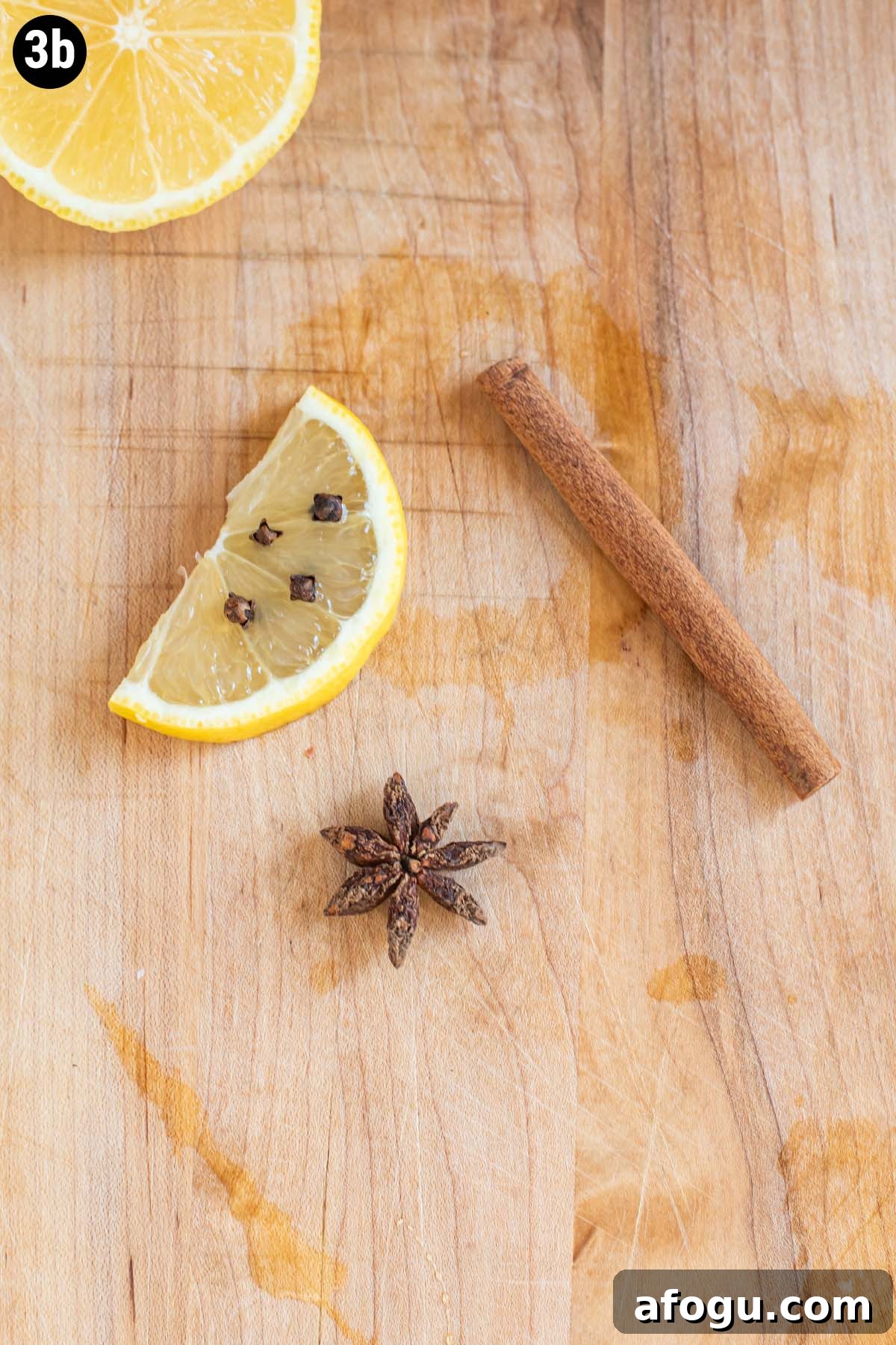 A cinnamon stick, star anise, and lemon slice with whole cloves on a cutting board.