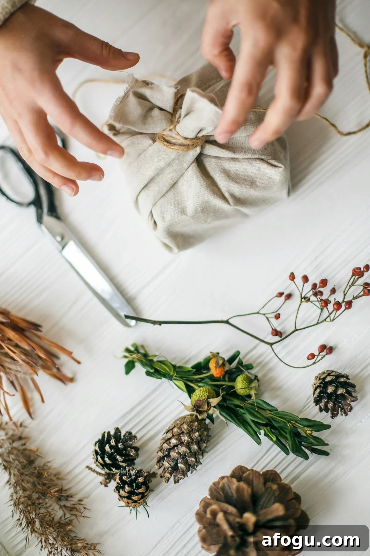 75 Minimalist Gift Ideas for a Clutter-Free Home 2 Top down look at two hands tying up a homemade gift with neutral linen fabric and twine, with other decorating supplies in the background