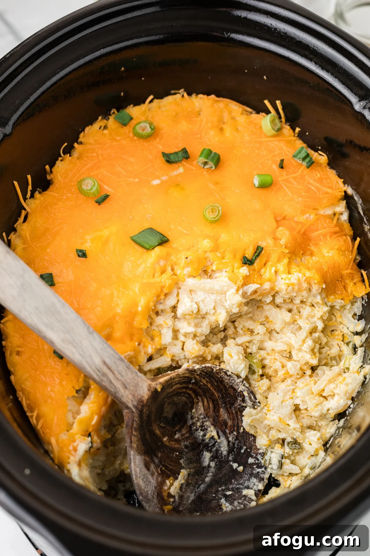 Slow cooker party potatoes with a large wooden spoon in the crockpot.