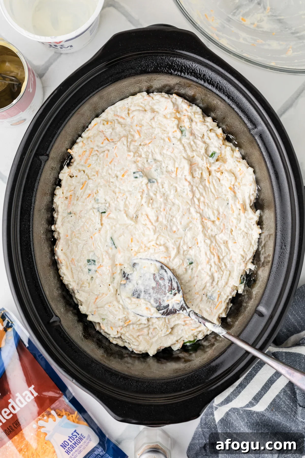 Party potatoes mixture in a crockpot with a spoon.