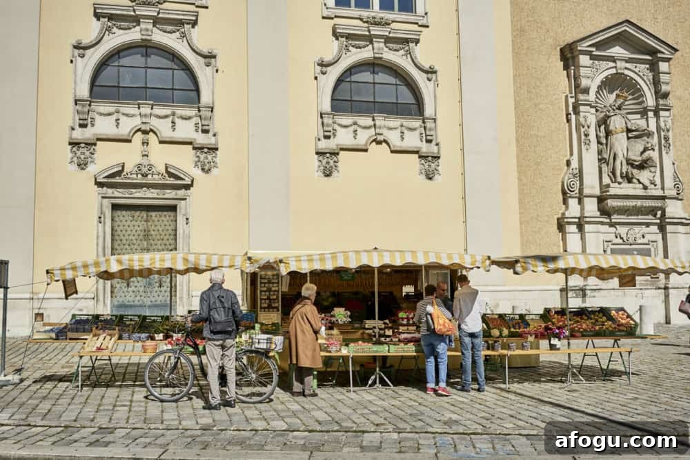 Top Vienna Markets: Where to Shop Local Food, Crafts & Gifts 2 Men and women buying goods from a small produce stand with yellow and white striped awnings in Vienna. It is on a cobble-stoned street with a pale yellow Beaux Arts style building in the background.