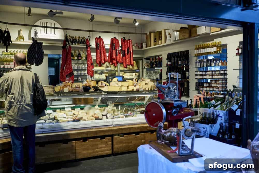 Top Vienna Markets: Where to Shop Local Food, Crafts & Gifts 14 A cheese and charcuterie stand at Naschmarkt in Vienna. A deli case holds a variety of cheeses and cured salamis hang from the ceiling. A meat grinder is in the foreground.
