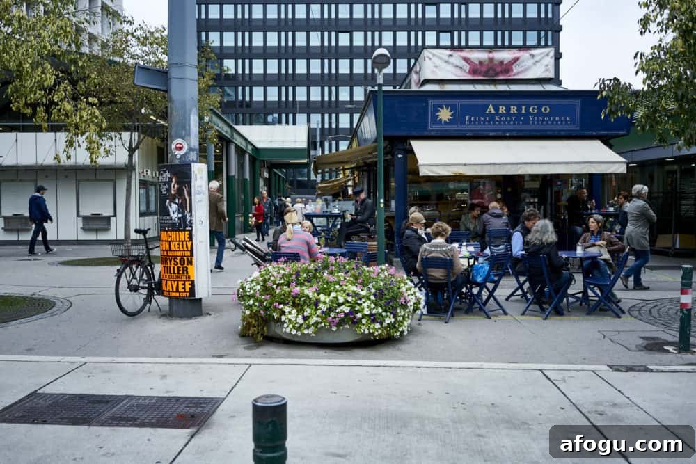Top Vienna Markets: Where to Shop Local Food, Crafts & Gifts 5 Arrigo coffee and wine bar at Rochusmarkt in Vienna. A blue square building with yellow and white striped awnings. Patrons sit outside at blue tables.