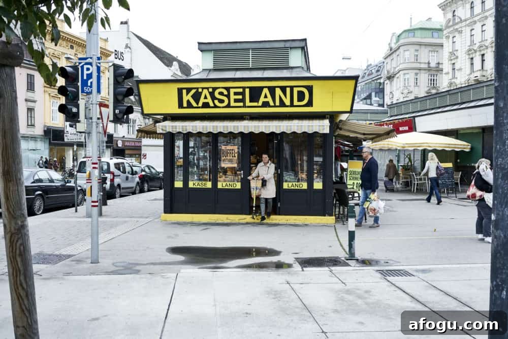 Top Vienna Markets: Where to Shop Local Food, Crafts & Gifts 8 Käseland shop at Rochusmarkt Vienna. A yellow and black building, a woman is exiting the front door with a scooter.
