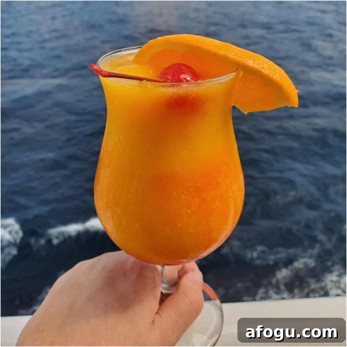 Blended kiss on the lips cocktail in a hurricane glass garnished with a cherry and orange slice