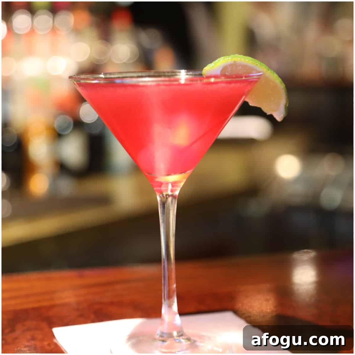 Bright red martini with a lime wedge in a martini glass on a white napkin