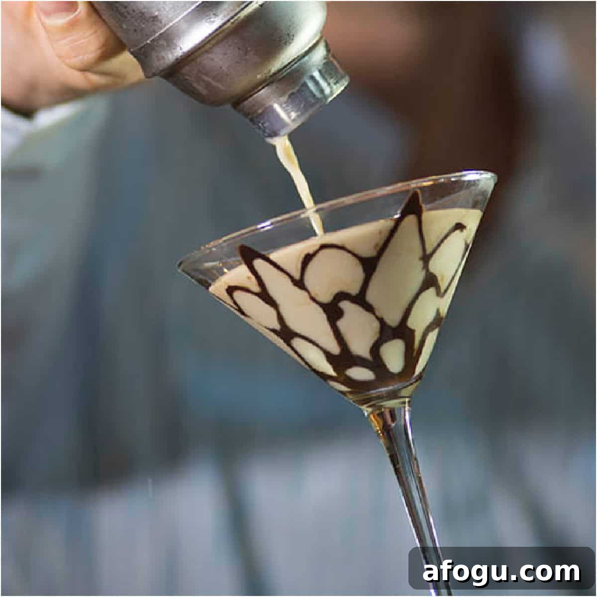 Tiramisu Martini pouring from a cocktail shaker into a martini glass with chocolate design.