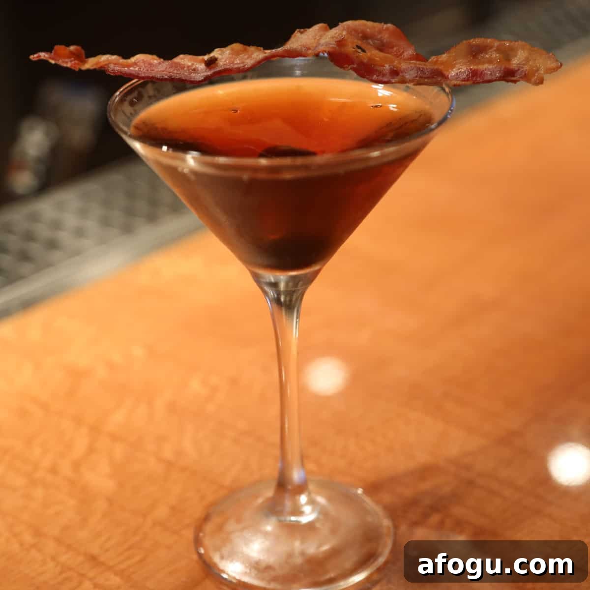 Bacon Manhattan in a martini glass with a slice of bacon for garnish