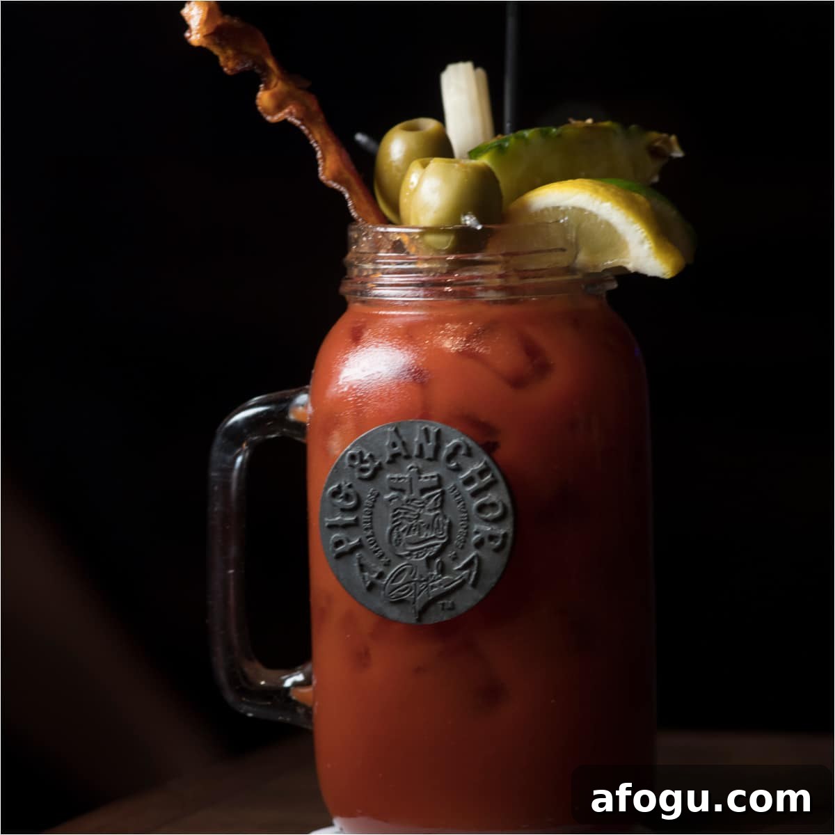 bloody mary cocktail in a large mason jar glass garnished with bacon, olives, and lemon