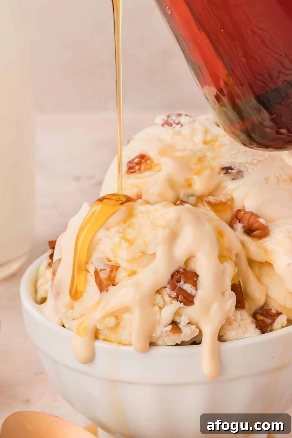 Maple syrup being poured on maple pecan ice cream in a bowl.