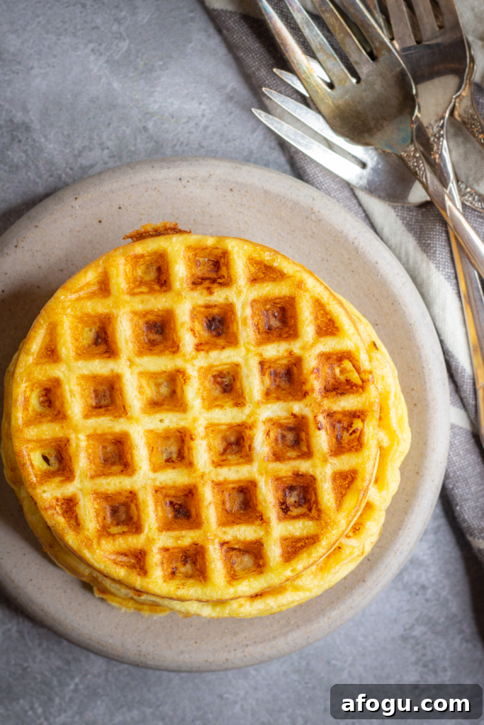 A stack of round chaffles on a stone plate on top of a gray marbled background. There is a white and gray striped linen beside the plate