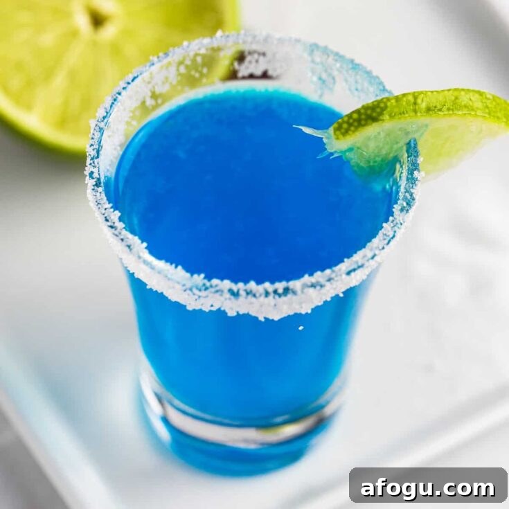 An overhead view of a blue kamikaze shot with a sugar rim, garnished with a slice of lime.