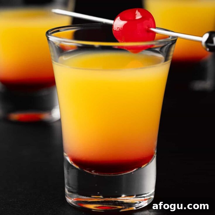 Three Tequila Sunrise Shots garnished with a maraschino cherry on a black background.